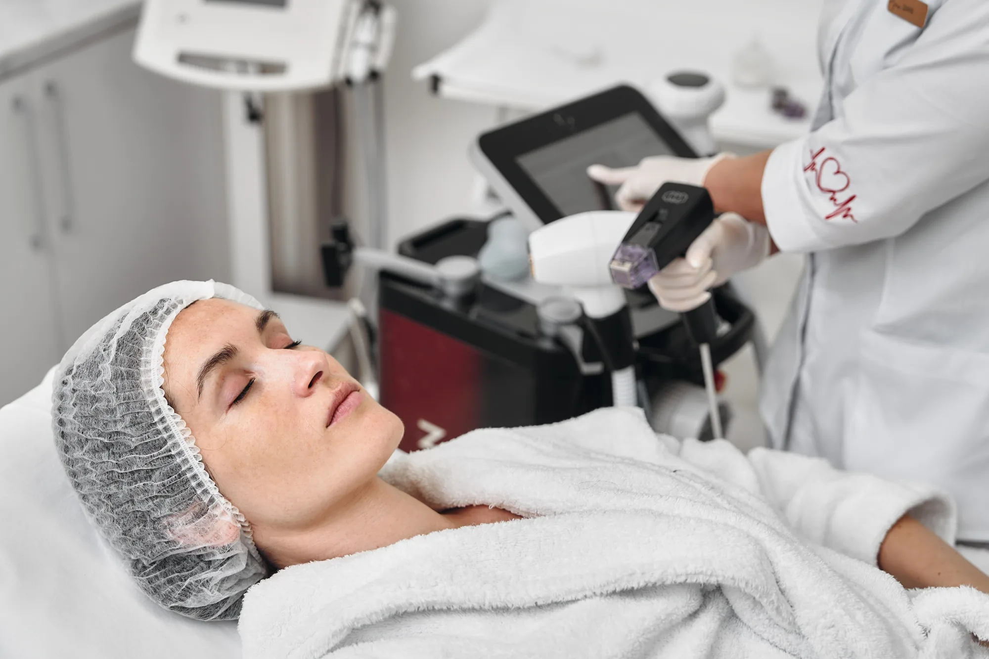 Woman lying down with closed eyes while a specialist sets up a RF lifting device